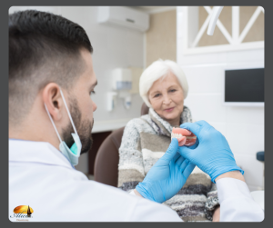 A dentist wearing blue gloves shows a set of dentures to an elderly woman during a denture exam and maintenance appointment in a dental office
